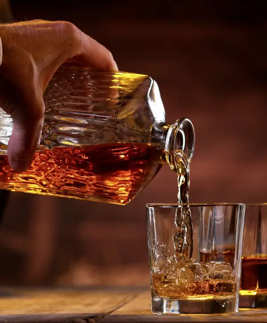 Hand pouring whisky from a crystal decanter into a glass with ice at Osiris Club bar.