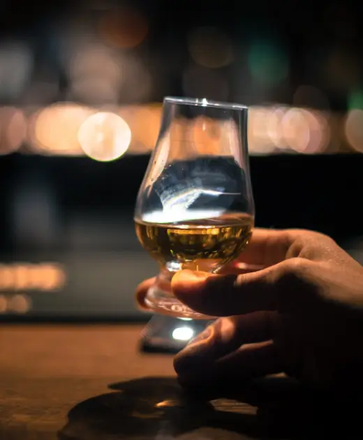 A close-up of a hand holding a glass of premium whiskey at the Osiris Club Stanmore bar with warm ambient lighting.