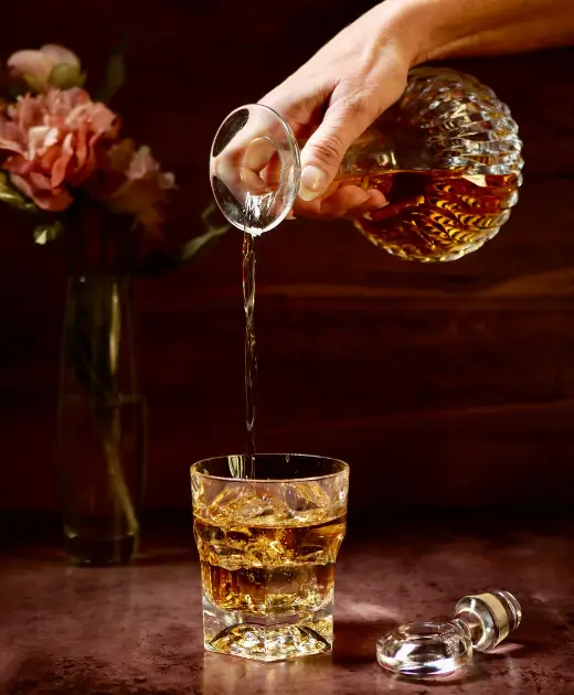 Whiskey being poured from a crystal decanter into a glass with ice on a bar counter at Osiris Club Stanmore.
