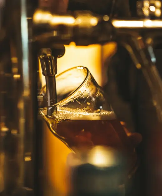 Close-up of golden draft beer being poured from tap into glass at Osiris Club Stanmore, showcasing quality drinks and bar service.