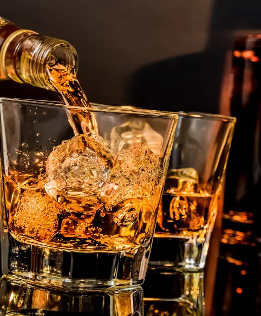 Golden whiskey being poured over ice cubes in a glass at Osiris Club Stanmore.