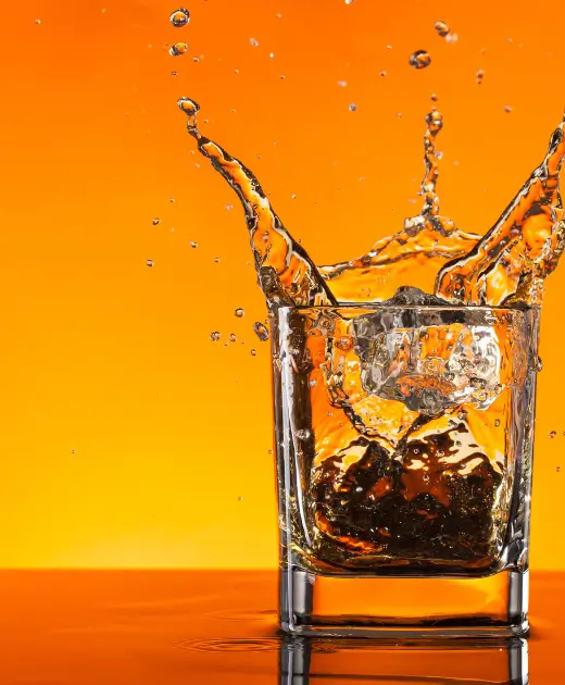 Refreshing whiskey splash with ice cubes in a clear glass against an orange background — Osiris Club signature drink photography for brand promotion.