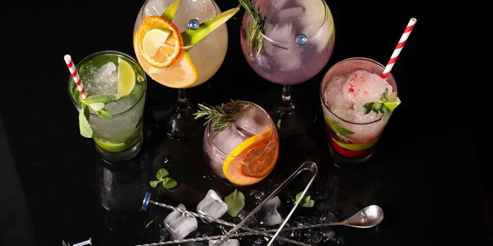 Vibrant colorful cocktails served with citrus slices, mint, and herbs on a glossy black surface at Osiris Club Stanmore, showcasing creative mixology and fresh ingredients.