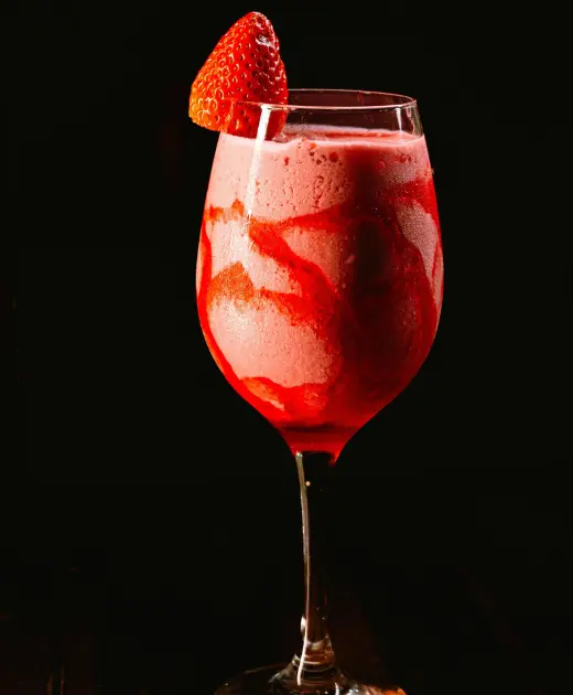 Frozen strawberry daiquiri cocktail served in a wine glass with a swirl of strawberry puree and a fresh strawberry garnish on the rim.