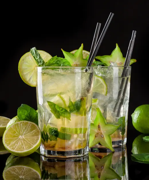 Refreshing mojito cocktail with lime, mint leaves, ice cubes, and starfruit slices served in two glasses with black straws.