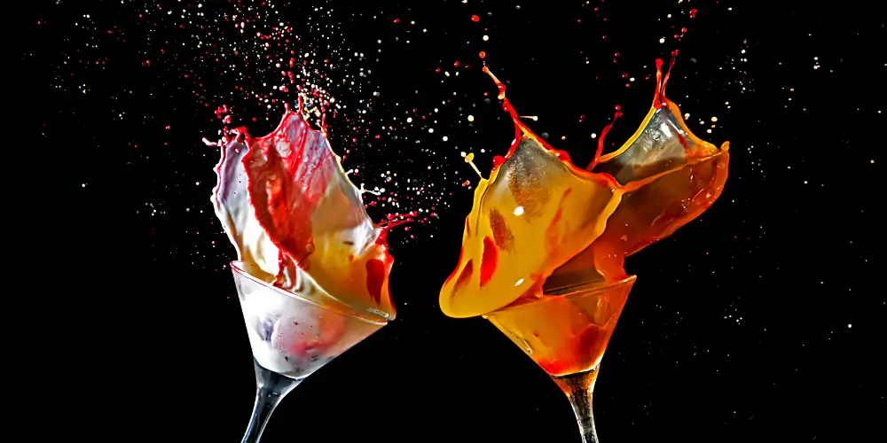 Two martini glasses clinking with vibrant red and orange cocktails splashing dramatically against a black background at Osiris Club Stanmore.